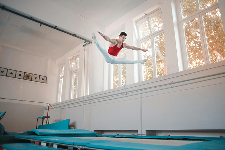 Person performing a gymnastics routine on a trampoline in a well-lit gym.
